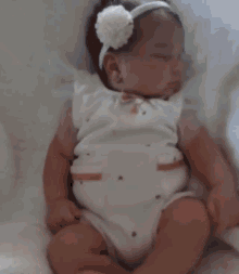 a baby wearing a white headband with a flower on it is sleeping on a bed