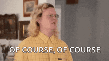 a man with long blonde hair and glasses is standing in a living room .