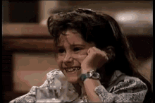 a young girl is smiling with her hand on her face while sitting at a table .