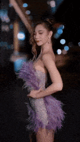 a woman in a purple feathered dress is standing in front of a building .