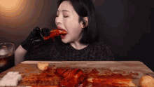 a woman wearing black gloves is eating a large piece of meat on a cutting board .