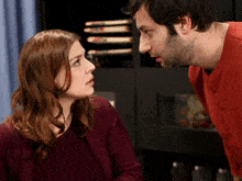 a man and a woman are looking at each other and the woman is wearing a red sweater