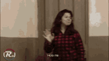 a woman in a red plaid shirt is waving and says hola me