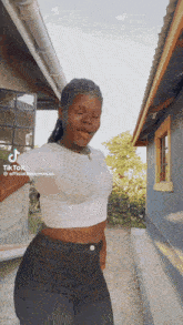 a woman wearing a white crop top and black jeans is dancing in front of a building ..