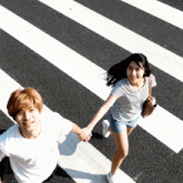 a man and a woman holding hands while crossing a street