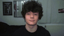 a young man with curly hair looks at the camera in front of a mirror