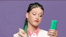 a woman with green braids is holding a green cell phone