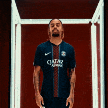 a man wearing a qatar airways jersey stands in a dark room
