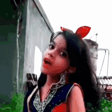 a little girl with a red bow on her head is standing in front of a building and making a funny face .