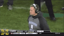 a man wearing headphones and a northwestern shirt watches a football game
