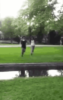 two women are running in a park near a bridge .