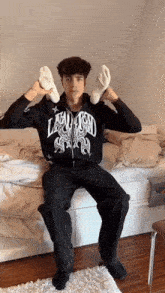 a man wearing a black jacket with the word laughed on it is sitting on a bed