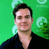 a man in a black shirt is smiling in front of a green wall with the word durrell on it