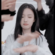 a woman with long black hair is surrounded by people 's hands .