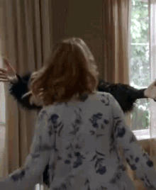 a woman in a floral shirt is standing in front of a window with her arms outstretched in a room .