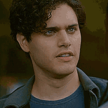 a close up of a man 's face with curly hair wearing a blue shirt and a gray jacket .