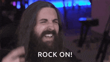 a man with long hair and a beard is making a devil horns sign with his hands .