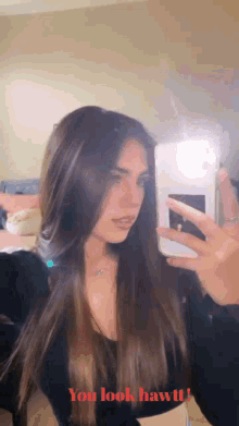 a woman taking a picture of herself in a mirror with the words " you look hawt " on the bottom