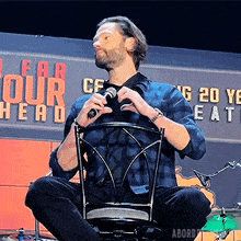 a man is sitting in a chair holding a microphone in front of a sign that says fear tour head