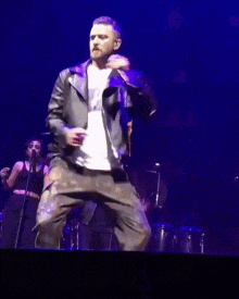 a man in a leather jacket singing into a microphone on a stage