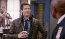 a man in a leather jacket and tie is talking to a police officer in a room .