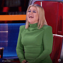 a woman in a green dress is laughing while sitting in a chair on nbc