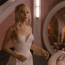 a woman in a white wedding dress stands in front of a mirror