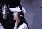 a woman wearing headphones and a white hat is singing into a microphone
