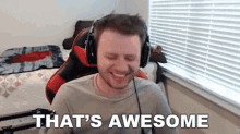 a man wearing headphones is smiling and saying `` that 's awesome '' while sitting in front of a window .
