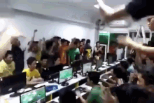 a group of people are standing in a room with computers and raising their arms in the air .