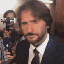 a man with a beard in a suit and tie is being interviewed by a reporter .