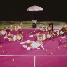 a group of women are laying on a pink tennis court with tennis balls around them