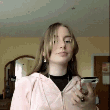 a girl in a pink hoodie holds a cell phone in her hand