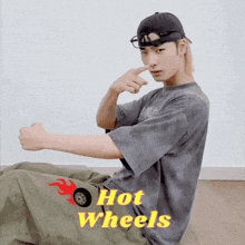 a man wearing a hat and goggles is sitting on the floor with hot wheels written on the bottom of his shirt