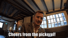 a man in a suit says cheers from the pickerell in front of a window