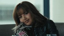 a woman in a black leather jacket sits at a table with flowers
