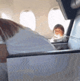 a woman and a child are sitting on an airplane looking out the window .