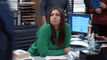 a woman in a green sweater is sitting at a desk