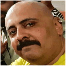 a bald man with a mustache is wearing a yellow shirt that says ' a ' on it
