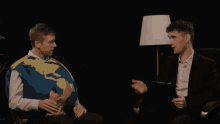a man in a suit is talking to another man in a sweater that looks like a globe .