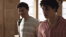 two young men standing next to each other with one wearing a pink shirt