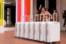 a woman in a bikini is standing in front of a row of white suitcases .