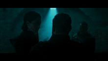 a man with a beard is standing in a cave in the dark looking at a woman .