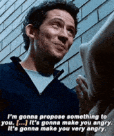 a man is talking to another man in front of a brick wall while wearing a hoodie .