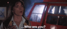 a woman is standing in front of a red vehicle and asking who are you