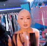 a woman with a shaved head is standing in a room with clothes hanging on a rack .