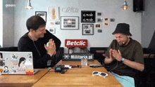 two men sitting at a table with a sign that says betclic on it