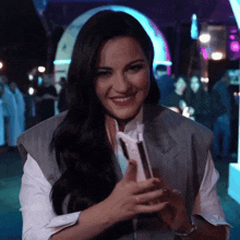 a woman in a gray vest is smiling while holding a cell phone