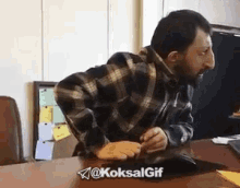 a man in a plaid shirt is sitting at a desk using a mouse .