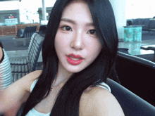 a woman with long black hair is wearing a white tank top and a necklace